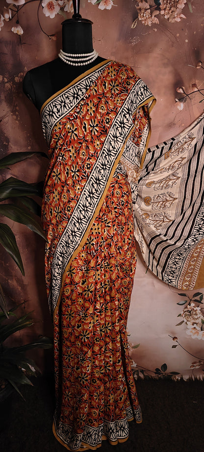 Modal Silk Saree – Reddish-Orange with Black & White Border and Golden Pallu Motifs saree with intricate patterns on a mannequin against a floral background
