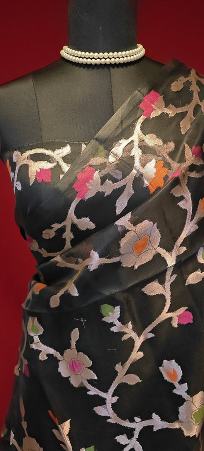 Black muslin blended silk saree with Jamdani weave and gold zari jaal, styled on mannequin showcasing the blouse piece and red background.