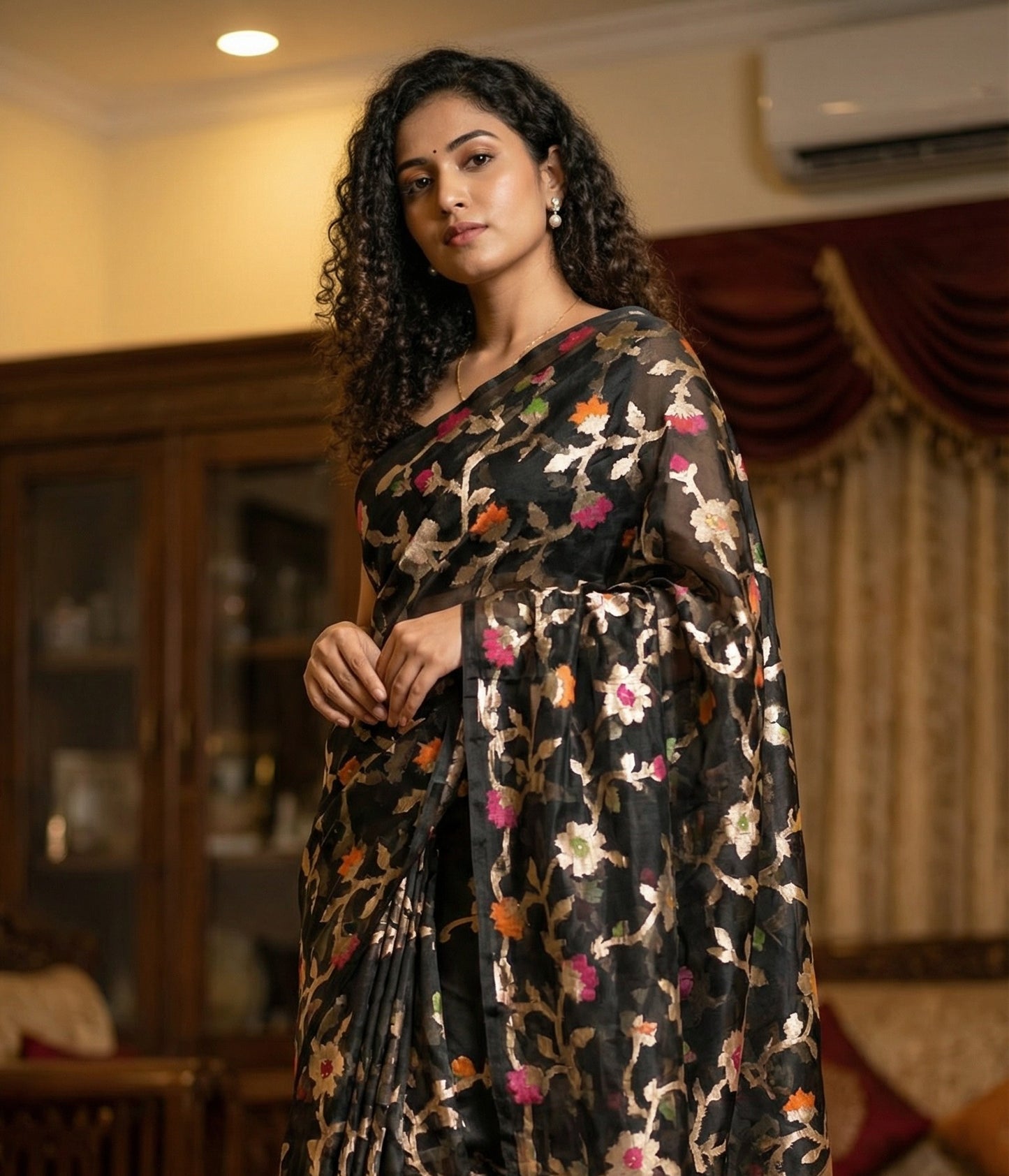 Woman wearing Black muslin blended silk saree with Jamdani weave and gold zari jaal. Low angle standing with soft chin tilt; makes saree look grand.