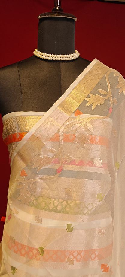 Cream muslin blended silk saree with golden border and pastel Jamdani motifs, styled on mannequin showcasing the blouse piece against a red background.