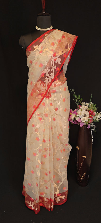 Cream muslin organza saree with red border and Jamdani floral embroidery, styled on mannequin with a flower vase and black background.
