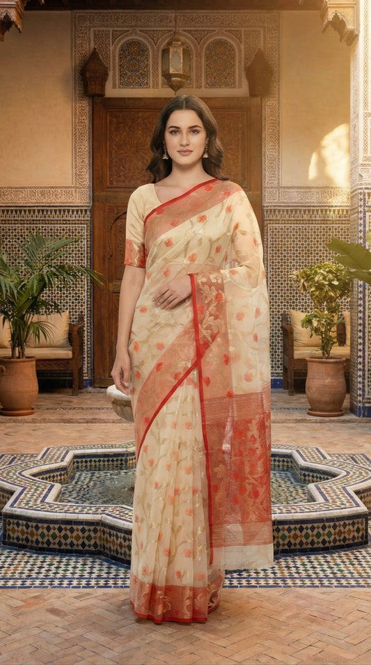 Woman in a cream muslin organza saree with red border and Jamdani floral embroidery, styled on mannequin with a flower vase and black background standing in an ornate indoor setting with plants and decorative tiles.