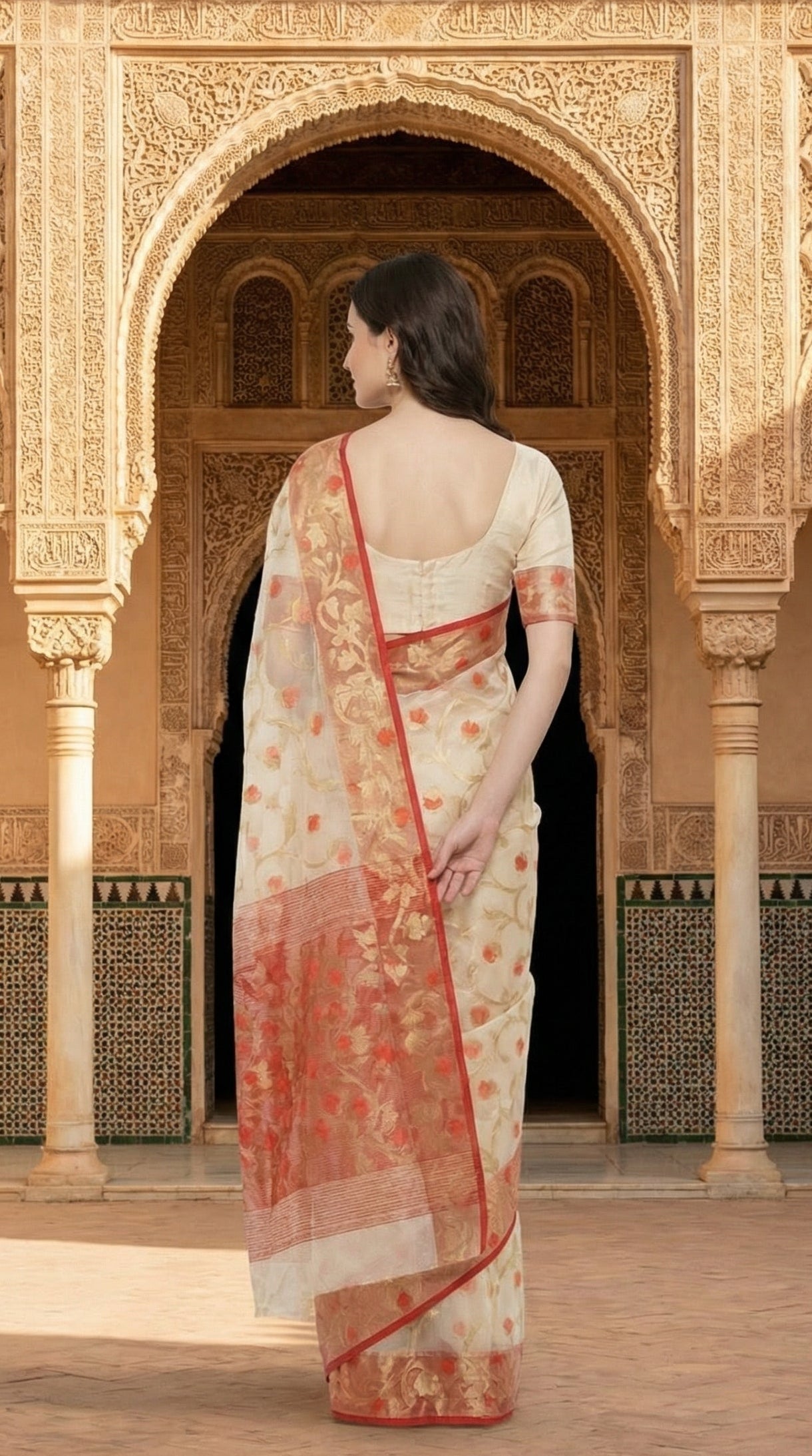 Woman in a cream muslin organza saree with red border and Jamdani floral embroidery, styled on mannequin with a flower vase and black background standing in a historic architectural setting with arched doorways.