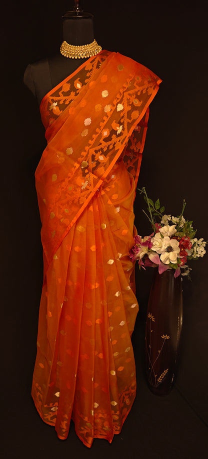Orange organza muslin saree with Jamdani weave and gold-silver Zari booti, styled on mannequin with flower vase against a dark background.
