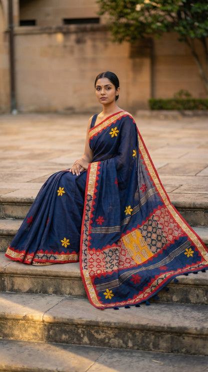 Woman in a navy blue linen cotton saree with traditional applique border, sitting on steps outdoors.