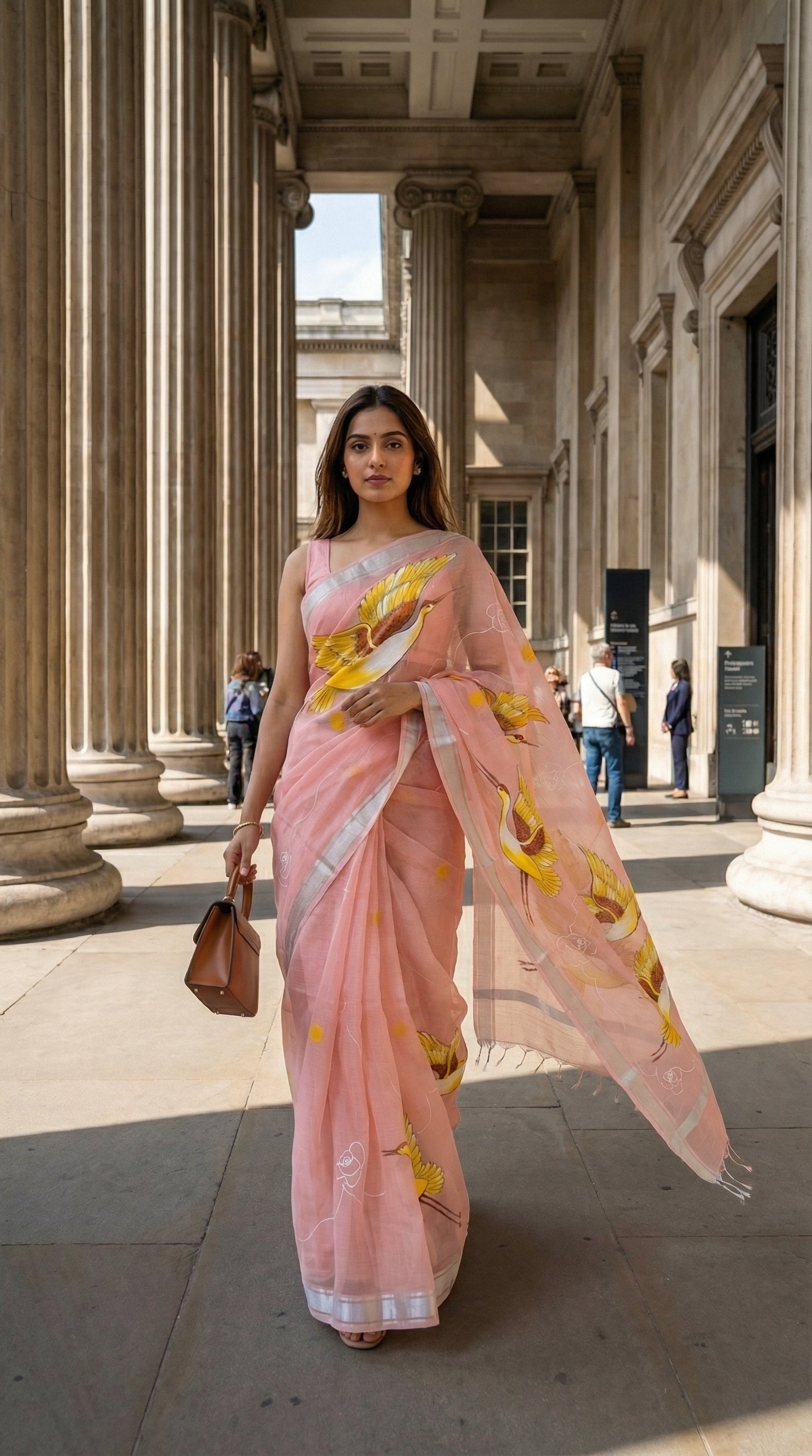 Woman in a peach-kota-doria-crane-saree, standing in front of classical architecture.