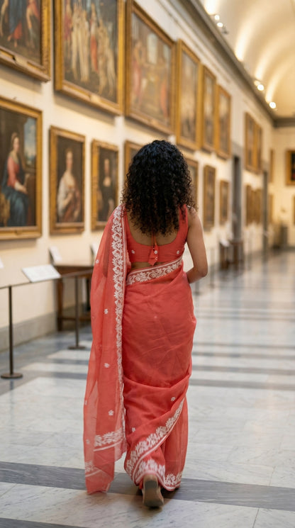 Woman in a peach-kota-doria-saree, walking through a museum with paintings on the walls.