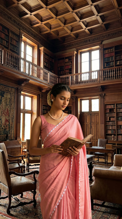 Woman in a pink saree reading a book in a library with wooden beams and bookshelves.