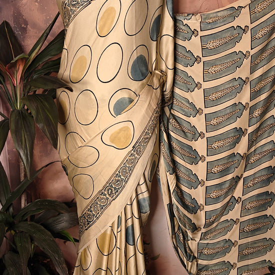 Ajrakh Modal Silk Saree – Beige with Golden & Olive Circular Motifs and Feather Pallu saree with intricate patterns on a mannequin against a floral background.