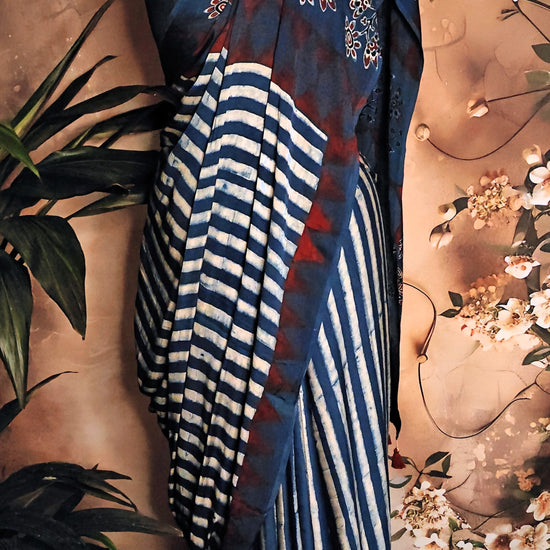 Ajrakh Modal Silk Saree – Blue & Maroon with White Floral Painted and Striped Pallu saree with floral and striped patterns on a mannequin against a floral background.