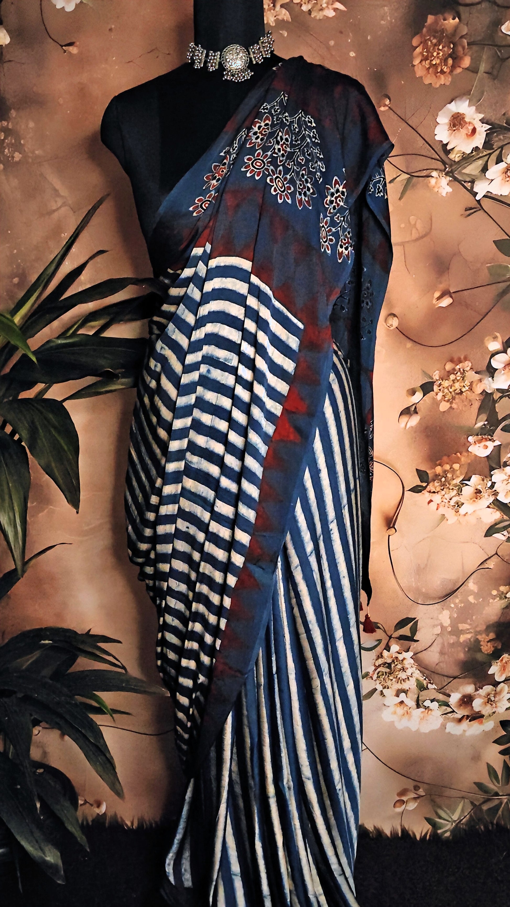 Ajrakh Modal Silk Saree – Blue & Maroon with White Floral Painted and Striped Pallu saree with floral and striped patterns on a mannequin against a floral background.
