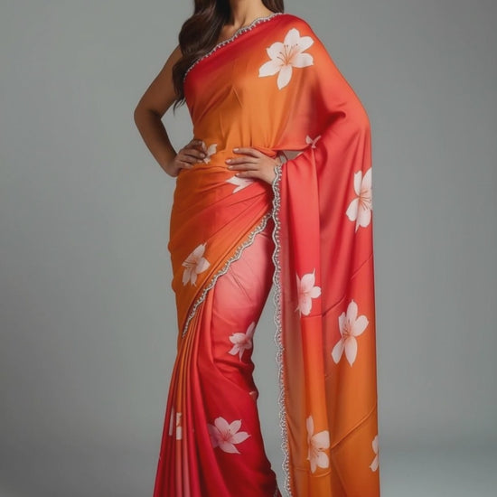 Woman wearing a red to orange gradient satin saree with white floral motifs and light zari border, elegant festive wear with floral patterns on a gray background.