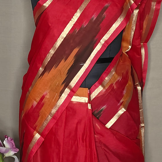 Magenta cotton saree with multicolor Ikat border and golden trim, folded with floral decor on a mannequin against a plain background.