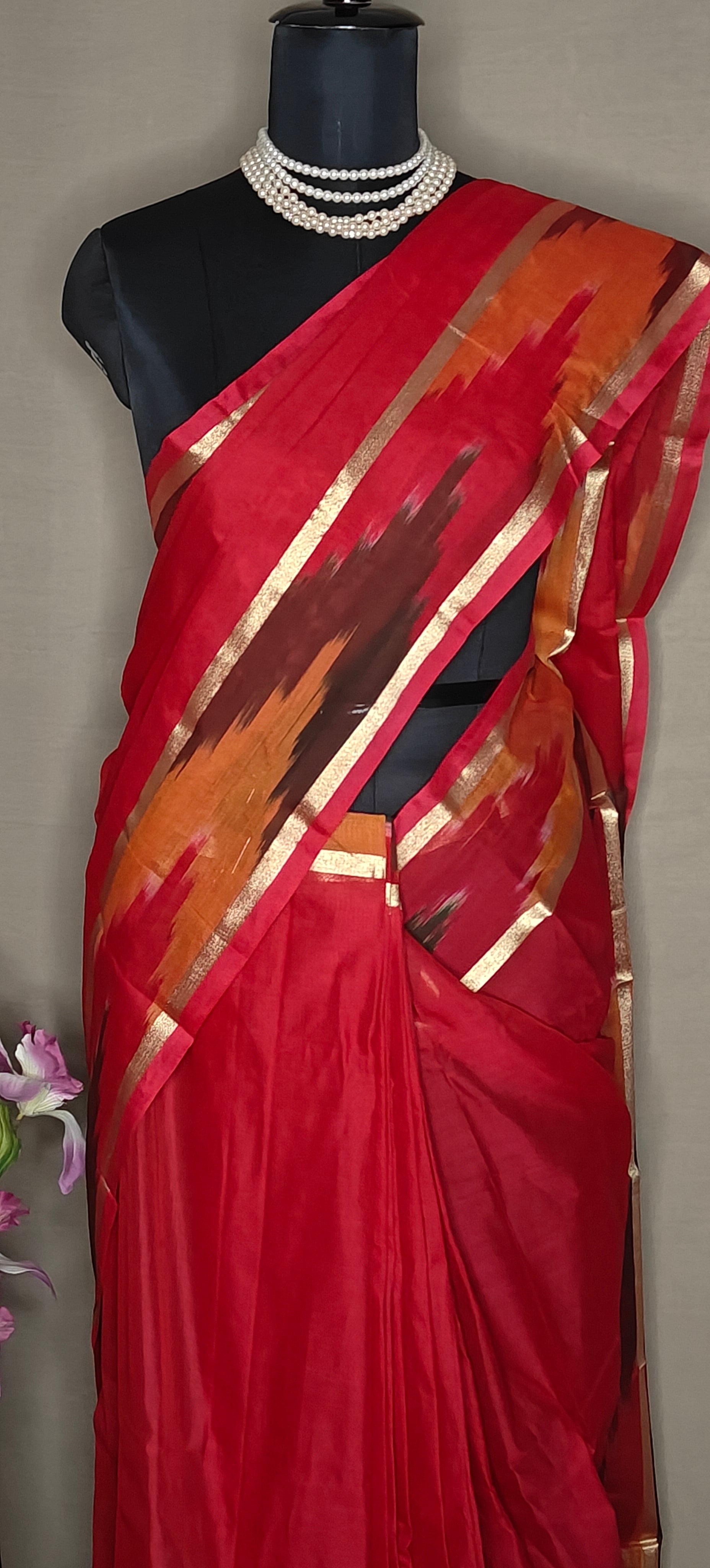 Magenta cotton saree with multicolor Ikat border and golden trim, folded with floral decor on a mannequin against a plain background.