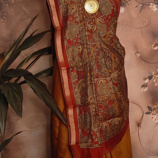 Maroon blended silk saree with Kalamkari-inspired floral and paisley digital print and broad golden border on a mannequin against a floral background.