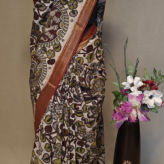 Brown silk saree with Kalamkari-inspired motifs and subtle golden border on a mannequin wearing a pearl necklace, against a neutral background.
