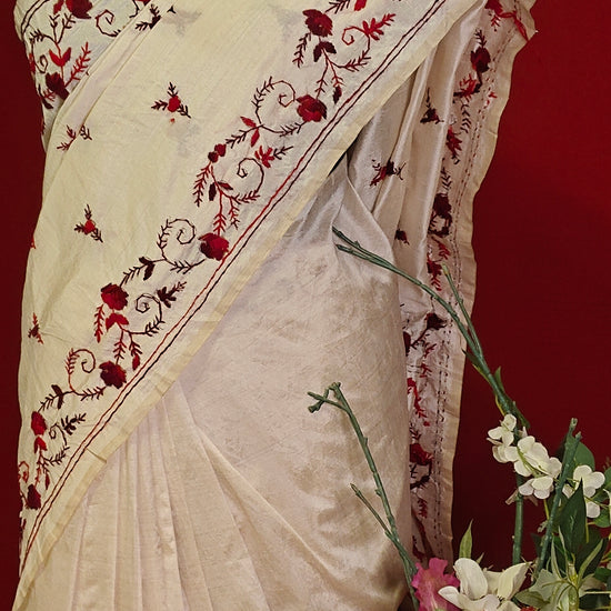 Handcrafted kantha stitched saree in cream with floral embroidery in maroon and red on a mannequin with a flower vase against a red background.