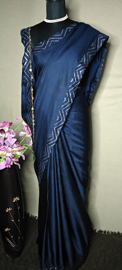 Blue silk saree with metallic zigzag border in gold and silver, displayed on mannequin with pearl necklace.