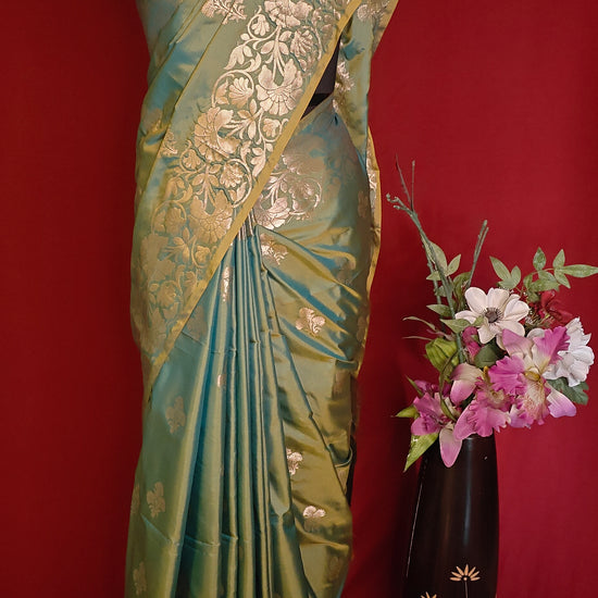 Emerald green silk blend saree with intricate woven detailing and elegant drape on a mannequin with a red background