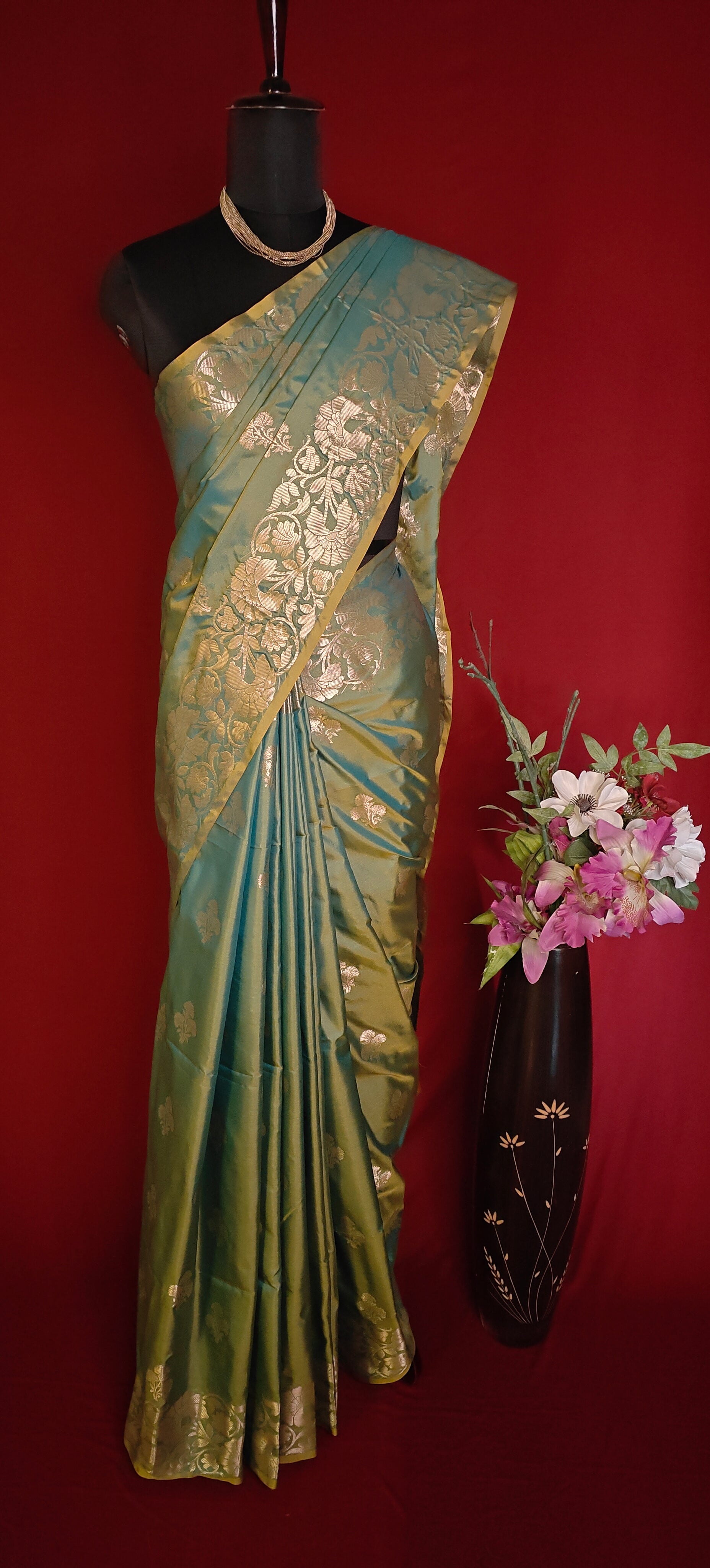Emerald green silk blend saree with intricate woven detailing and elegant drape on a mannequin with a red background