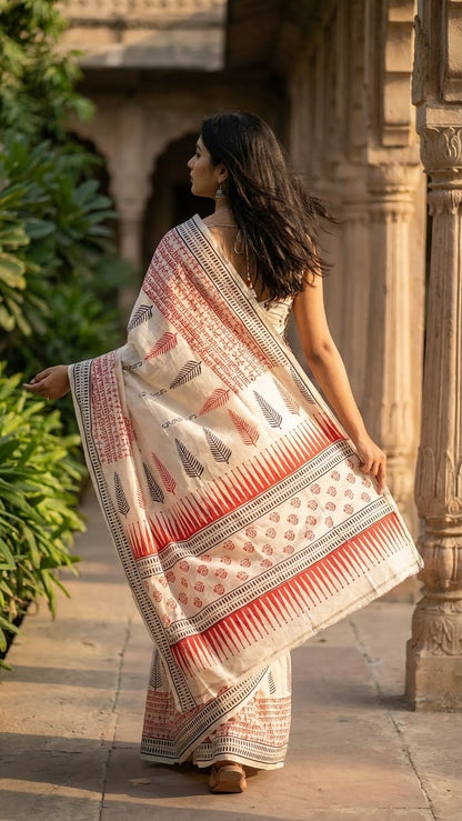 Woman holding a pure Bishnupuri silk saree in white with red and black printed motifs inspired by traditional Indian art with a pattern in an outdoor setting.