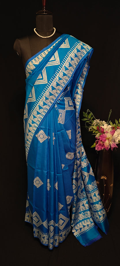 Pure bishnupuri silk saree in royal blue with white digital print motifs and geometric border, styled on mannequin with flower vase against black background.