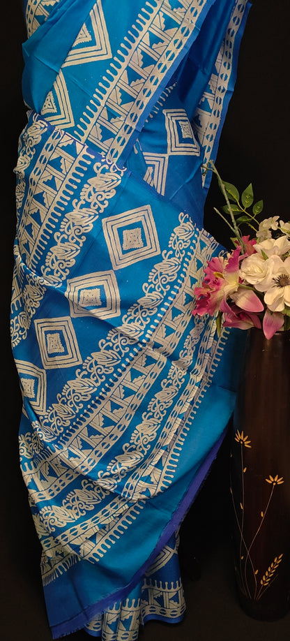Pure bishnupuri silk saree in royal blue with white digital print motifs and geometric border, styled on mannequin with flower vase, showcasing the pallu of the saree against black background.