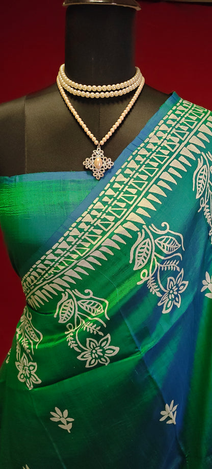Pure bishnupuri silk saree in dual tone green and blue with white floral motifs and elegant border draped on a mannequin showcasing the blouse piece against red background.
