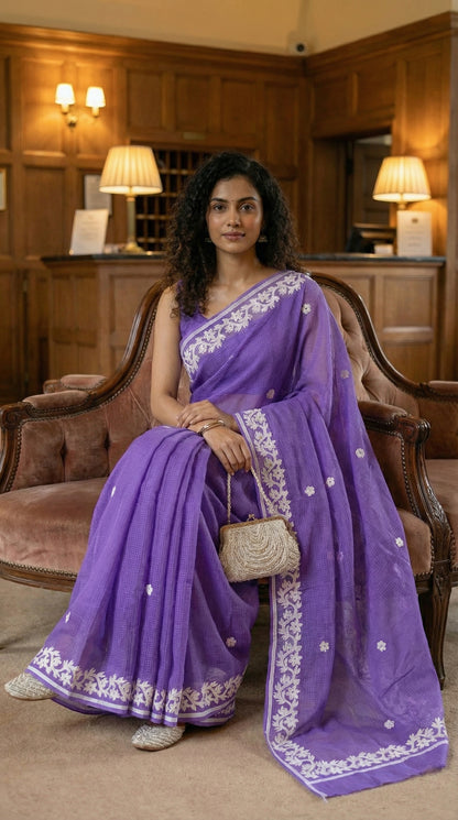 Woman in a purple-kota-doria-saree, sitting on a chair in an elegant room.