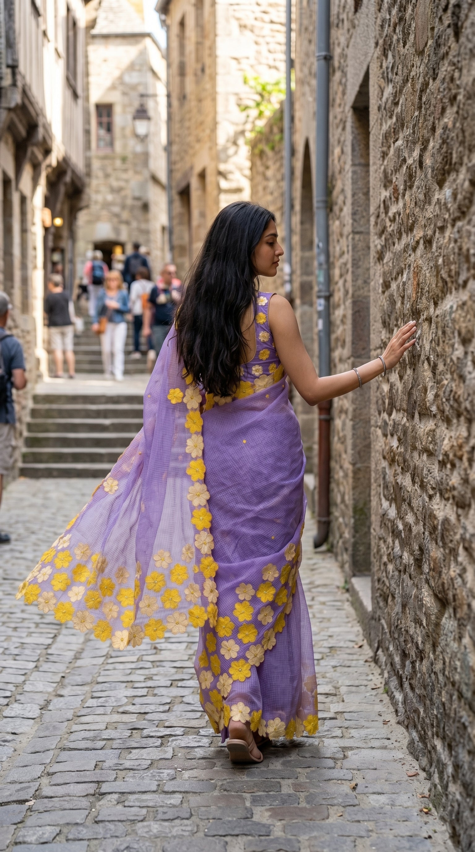 Woman in a purple-mirror-work-kota-saree, walking down a stone alleyway.
