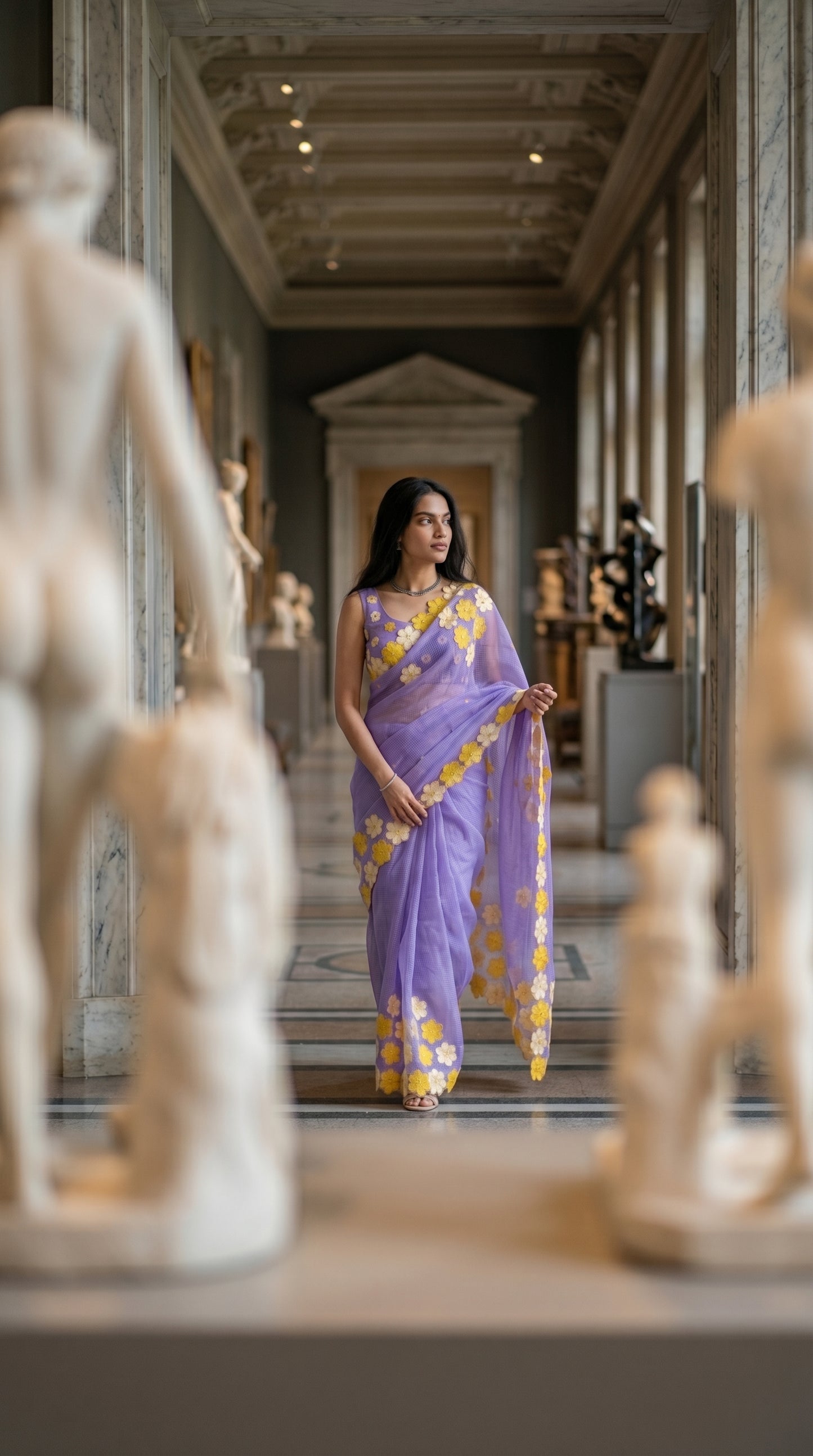 Woman in a purple-mirror-work-kota-saree, standing in an elegant hallway with classical statues.