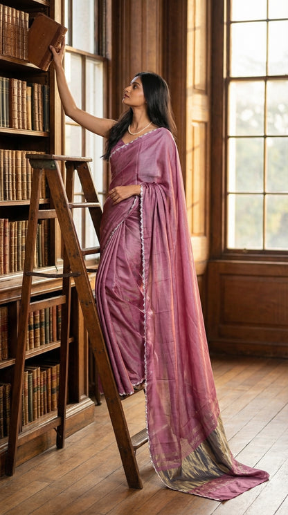 Woman in a rose-pink-modal-silk-saree-lagdi-patta-pallu, standing on a ladder in a library and picking a book to read.