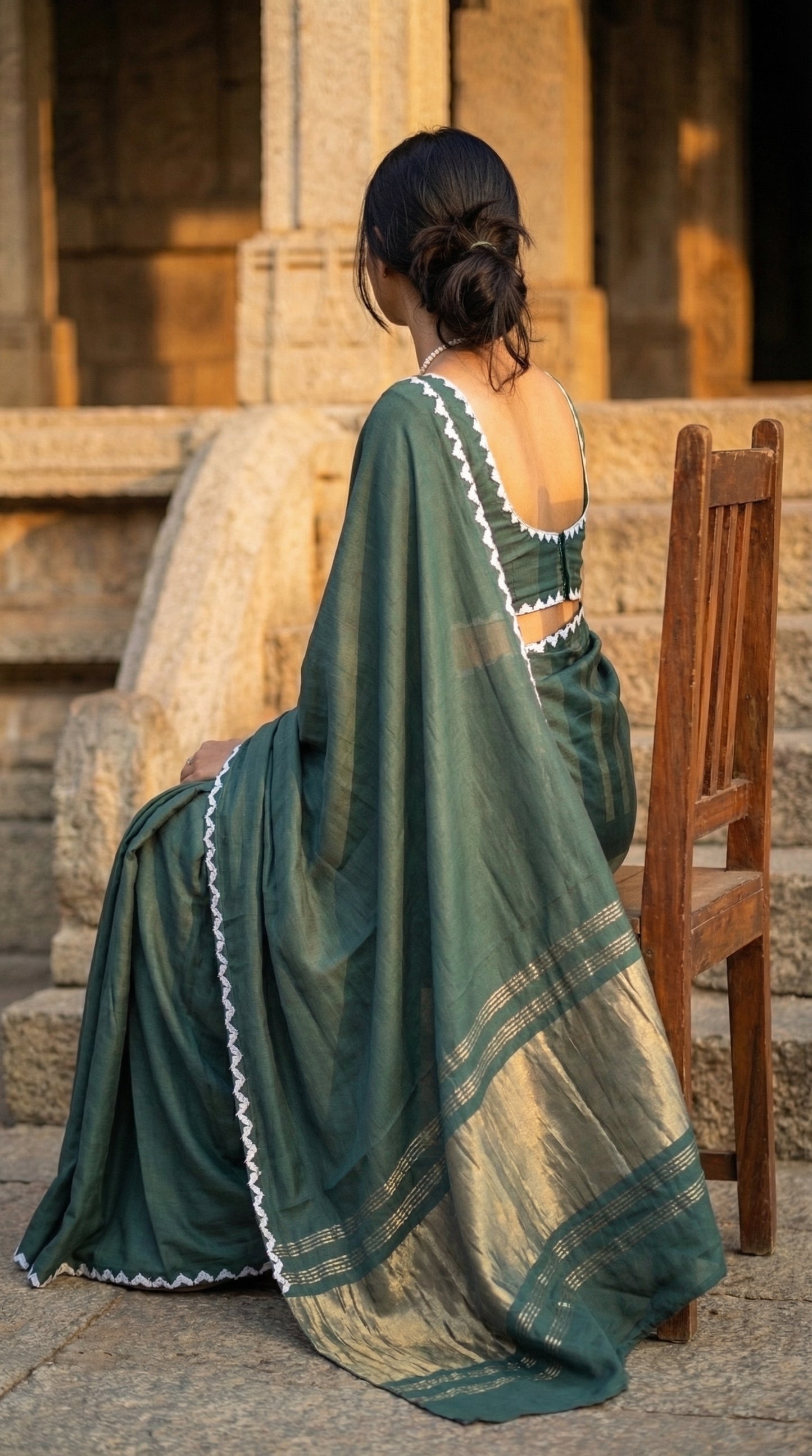 Woman in a sage-green-modal-silk-saree-lagdi-patta-pallu, sitting on a wooden chair.