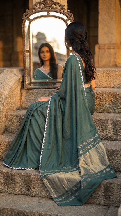 Woman in a sage-green-modal-silk-saree-lagdi-patta-pallu, sitting on steps, looking at herself in a mirror.