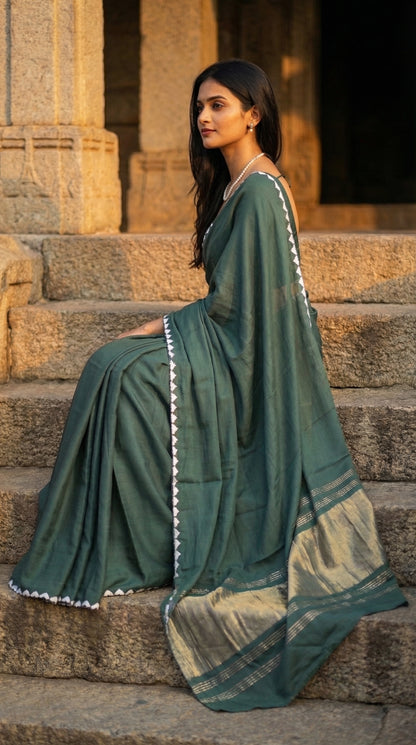 Woman in a sage-green-modal-silk-saree-lagdi-patta-pallu, sitting on steps.