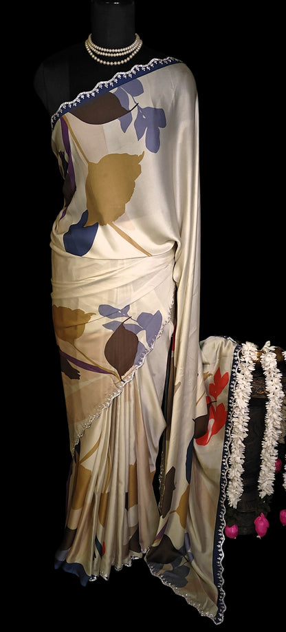 Beige satin-georgette saree with abstract floral prints and lace border, lightweight ethnic wear for festive occasions.