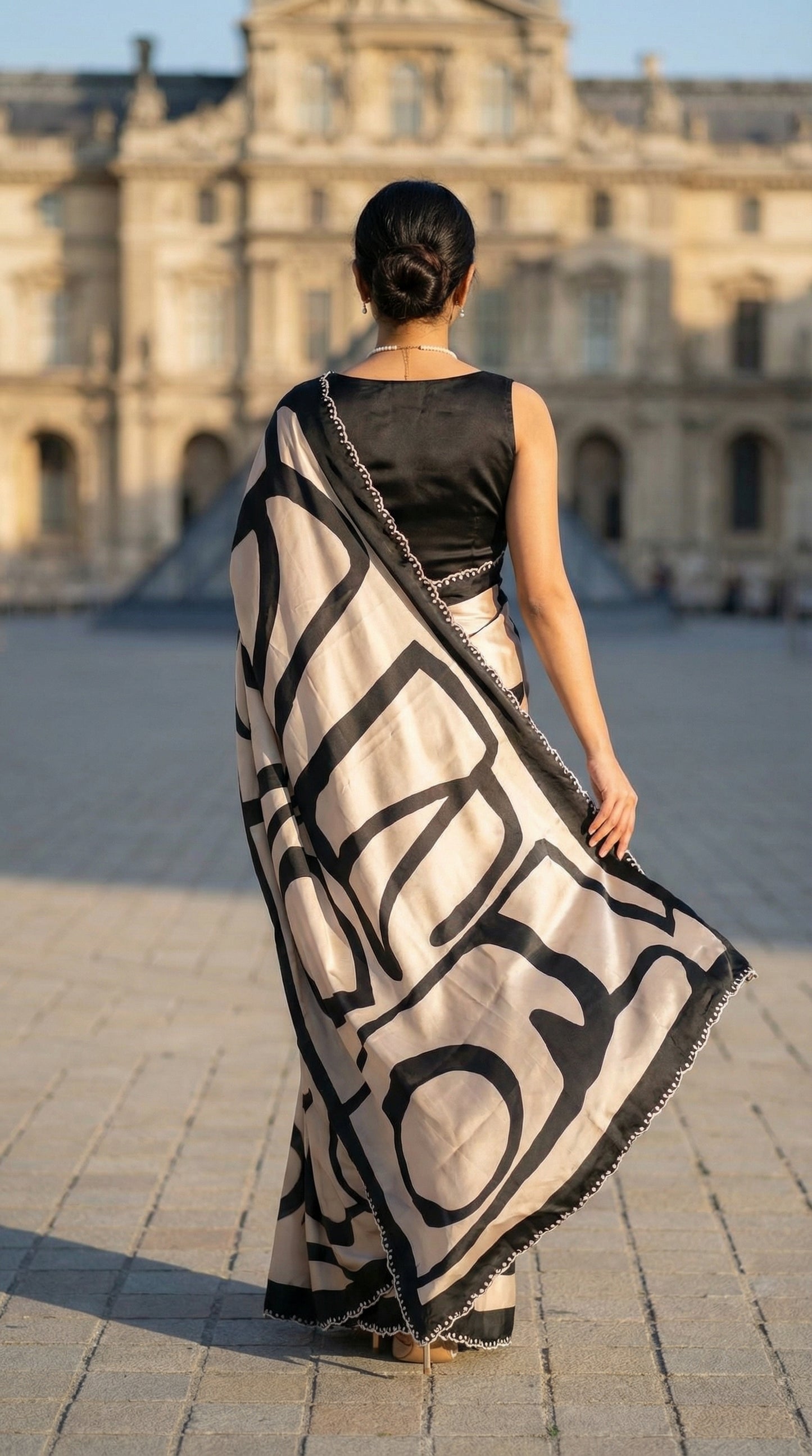 Woman in a Black satin-georgette saree with abstract line motifs on white base and subtle embellishments, in front of a large building.
