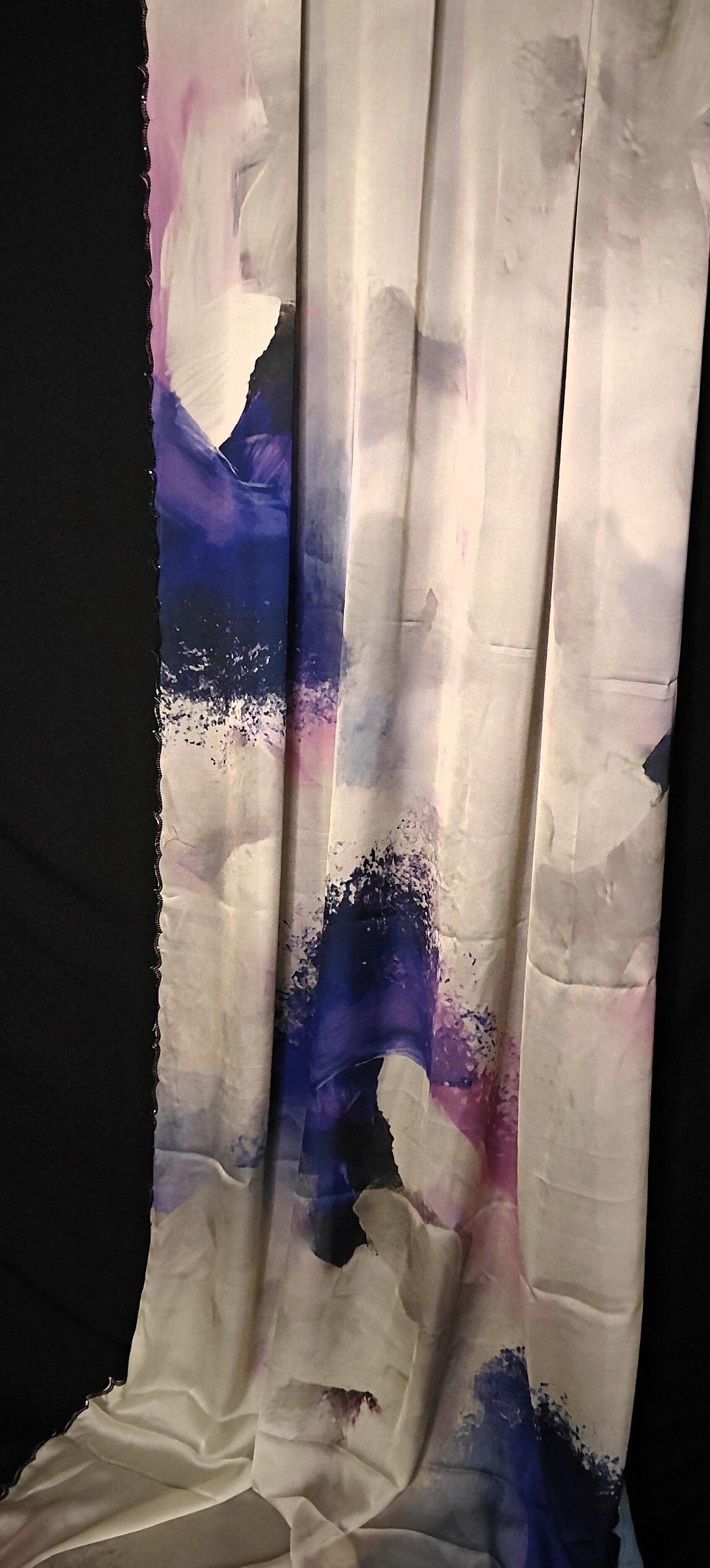 White satin-georgette saree with blue abstract brushstroke design and scalloped embellished border, elegant ethnic wear.
