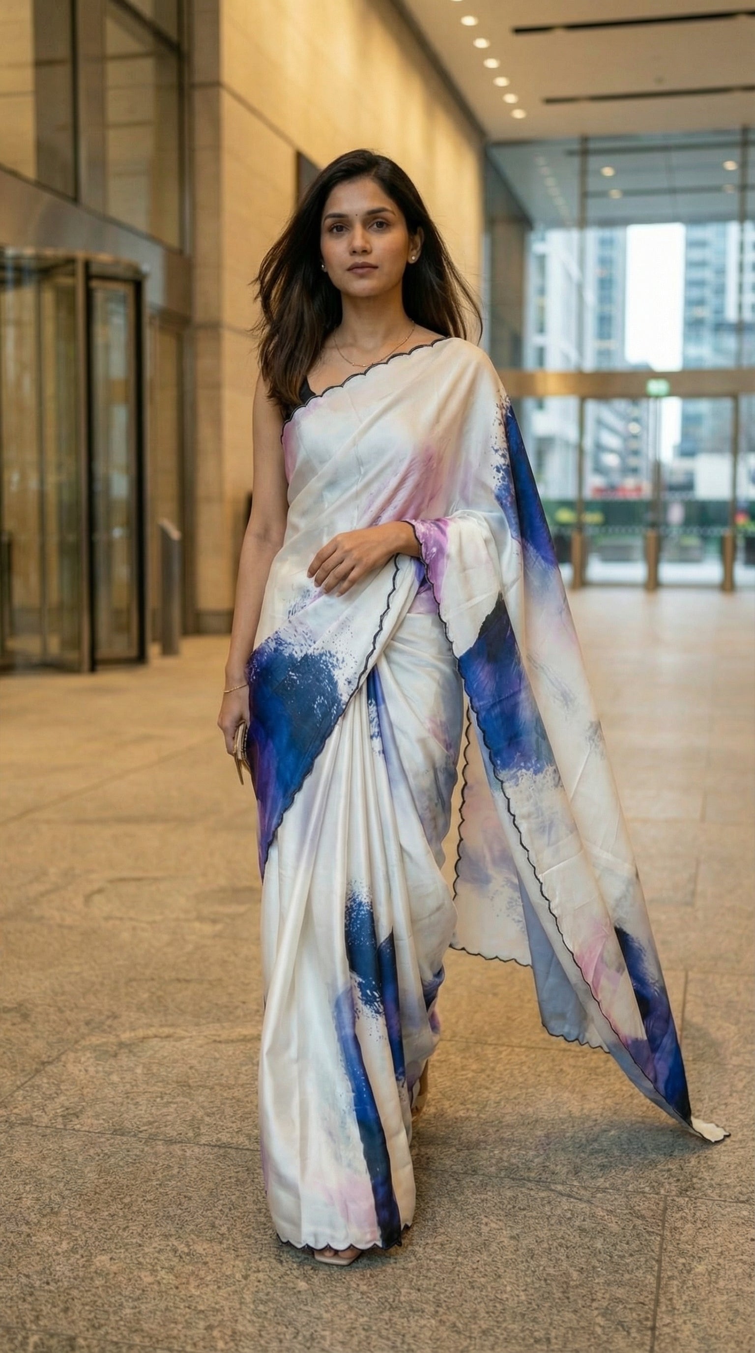 White satin-georgette saree with blue abstract brushstroke design and scalloped embellished border, in an indoor setting.