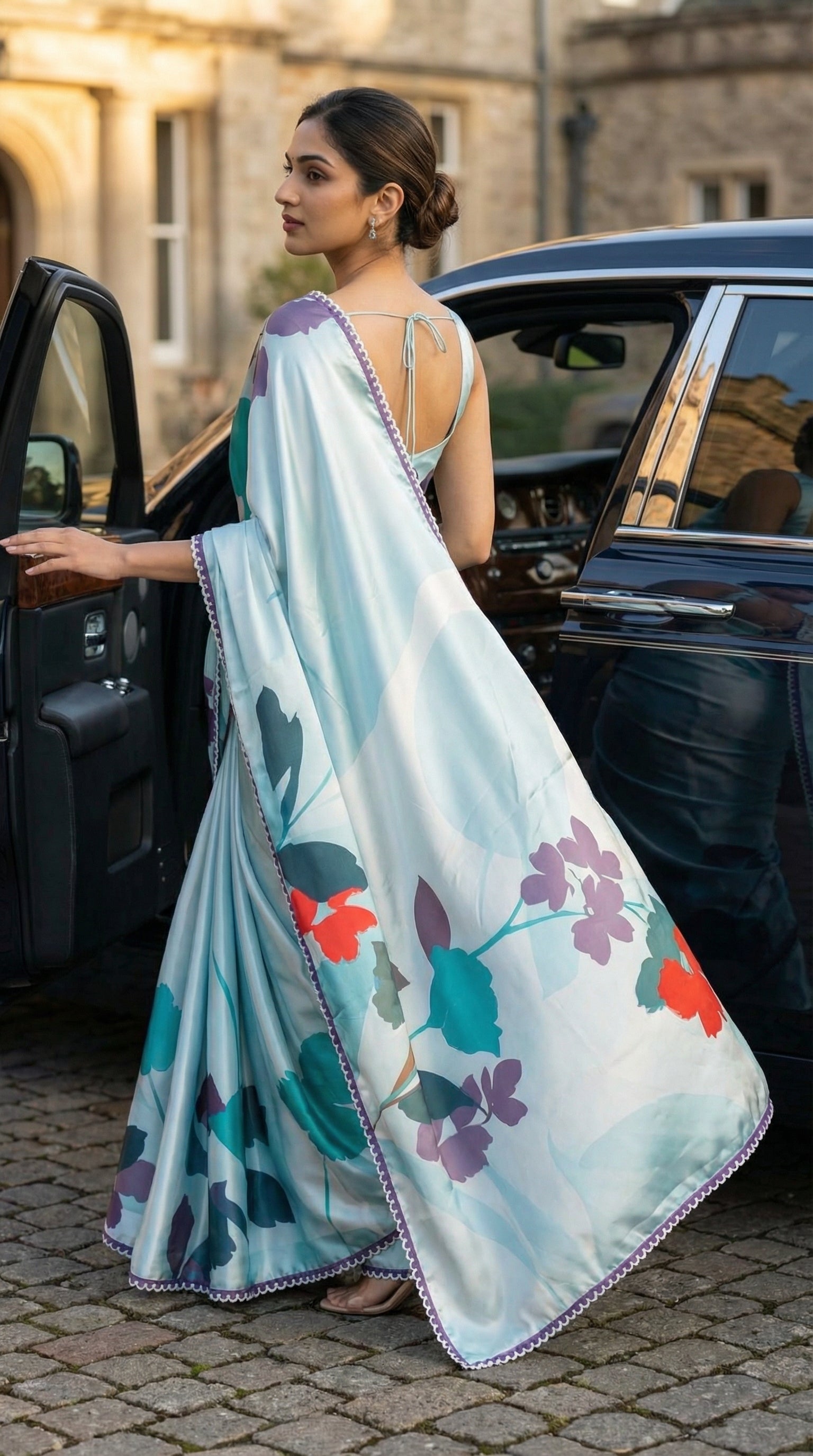 Woman in a Blue satin-georgette saree with multicolor floral design and lace border, getting out of a car.