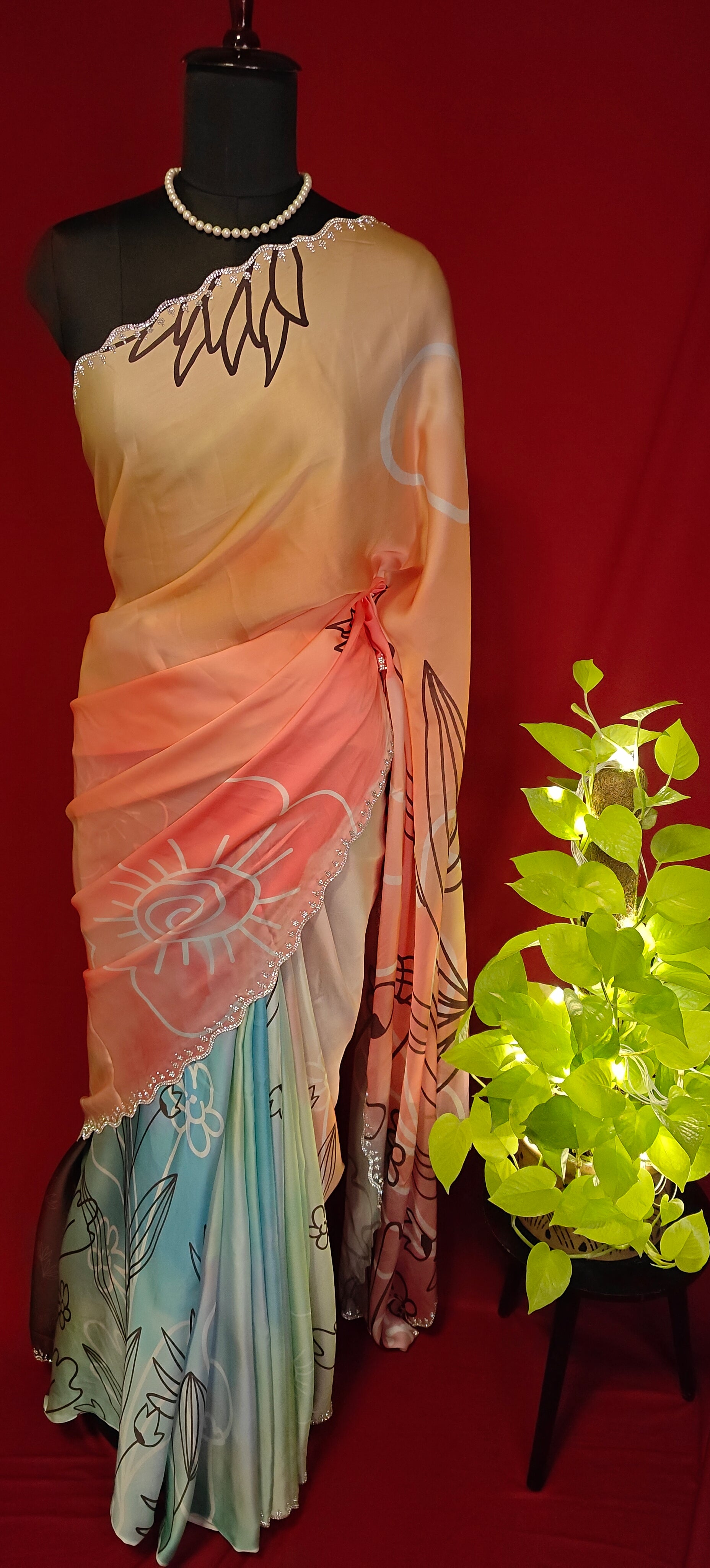 Multicolour satin georgette saree with abstract floral print and silver scalloped border on a mannequin with a red background and plant.