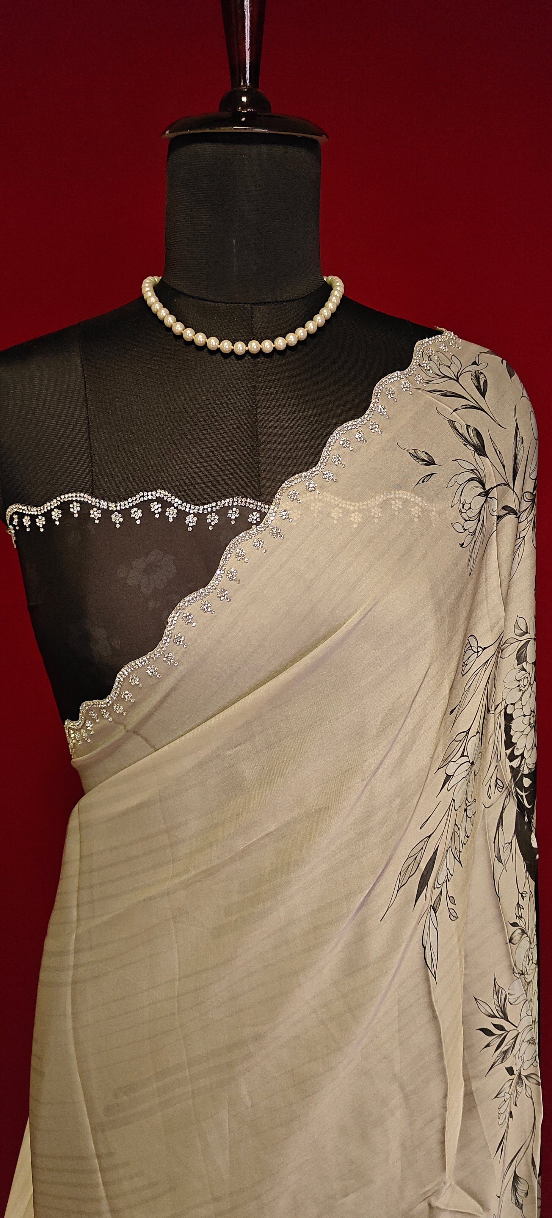 Black and white satin saree with abstract floral print and white pallu, styled on mannequin showcasing the blouse piece in black and silver motif border against red background.