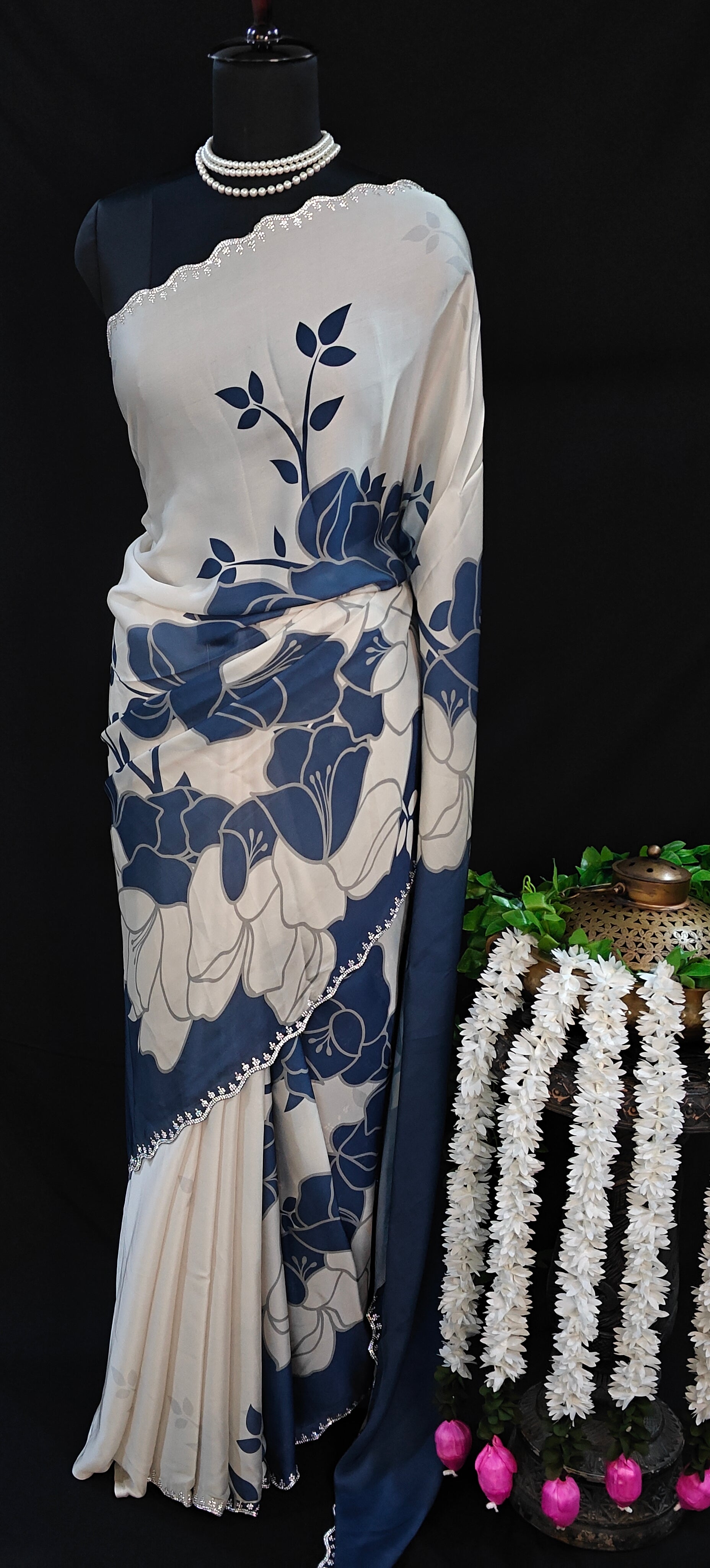Blue satin saree with bold white floral motifs and scalloped embellished border, elegant ethnic wear for festive occasions.
