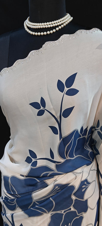Blue satin saree with bold white floral motifs and scalloped embellished border, elegant ethnic wear for festive occasions.