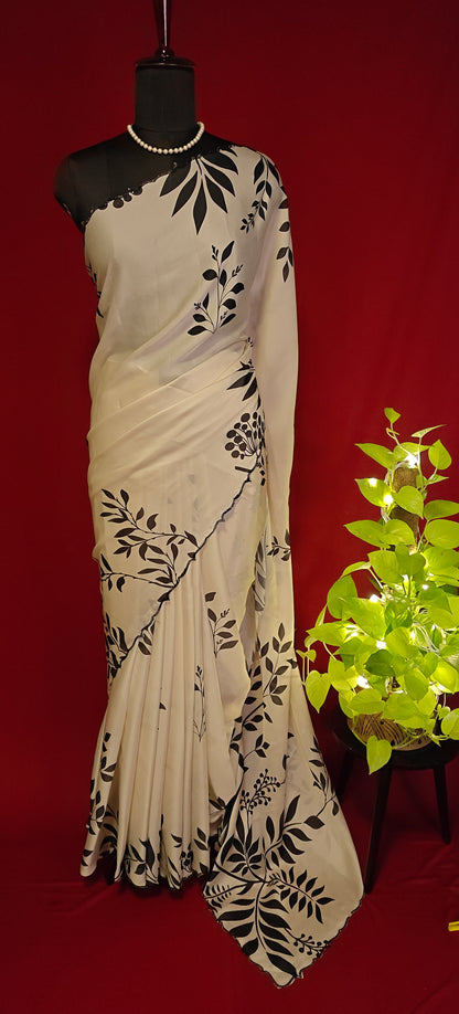 Cream satin saree with black leaf print and black motif border, styled on mannequin with plant against a red background.