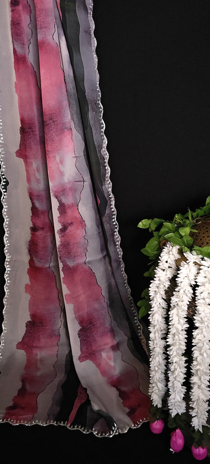 Pink satin saree with abstract print and scalloped silver border next to a plant with white flowers on a black background.