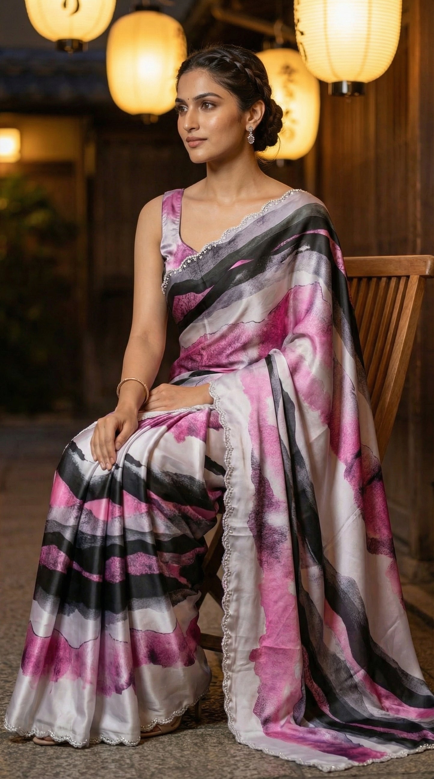 Woman in a Pink satin saree with abstract print and scalloped silver border, with a blurred background.