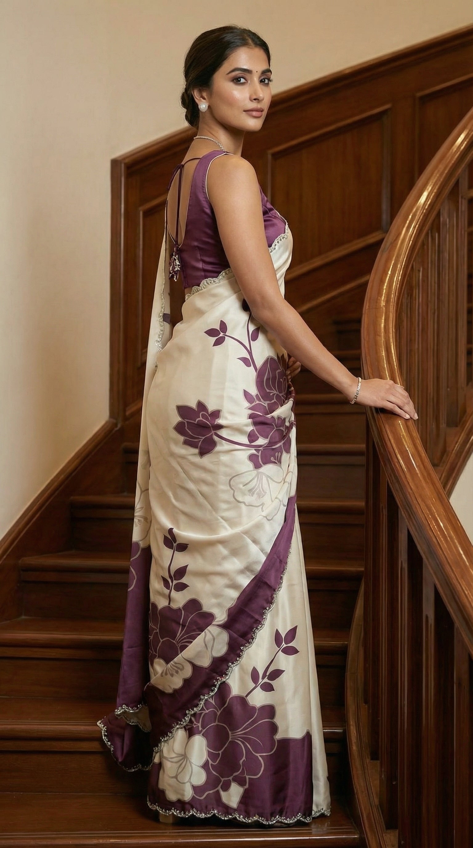 Woman in a Wine red satin saree with large floral patterns and scalloped border, standing on a staircase.