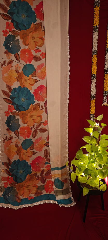 Cream satin chiffon saree with blue floral print and silver scalloped border hanging along with decorative items against red background.