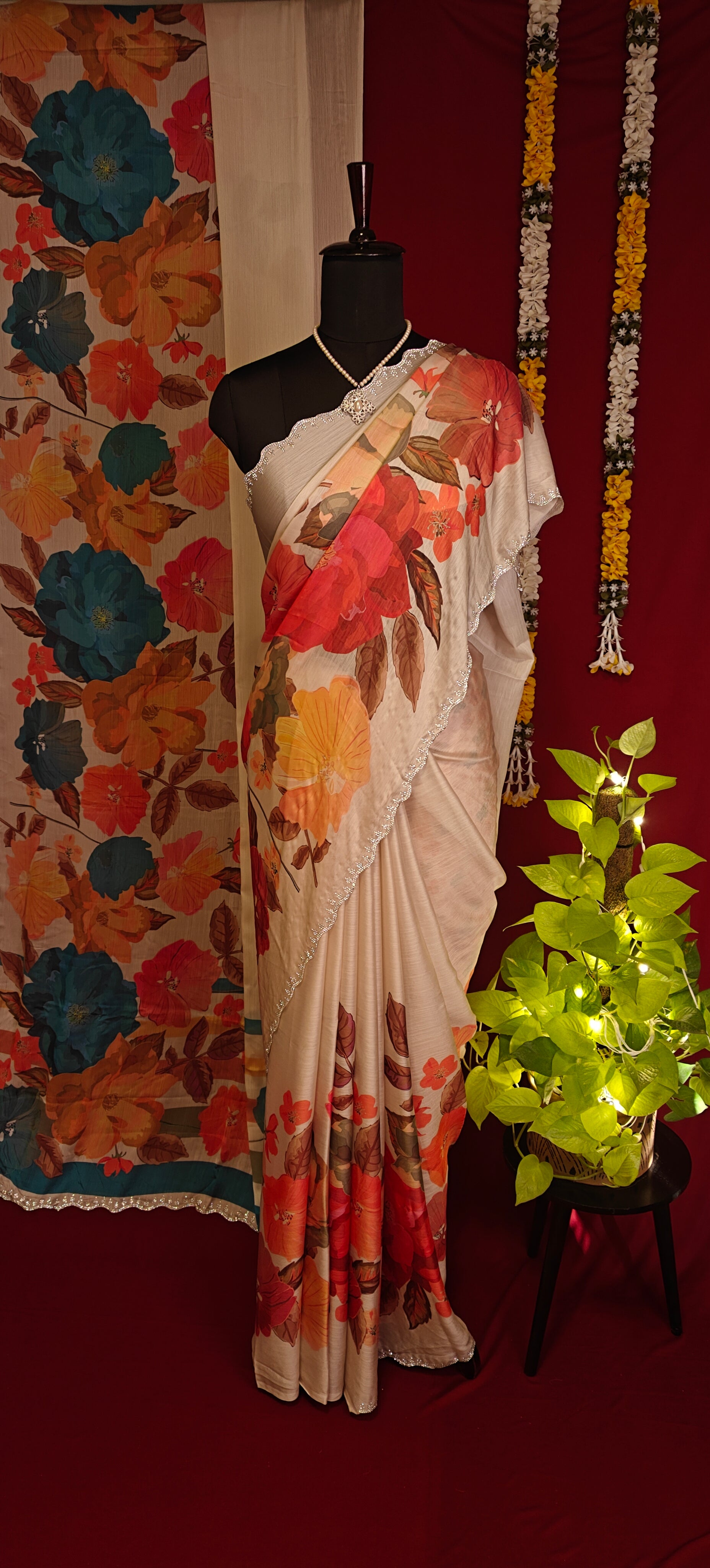 Cream satin chiffon saree with orange floral print and silver scalloped border and decorative items in the background.